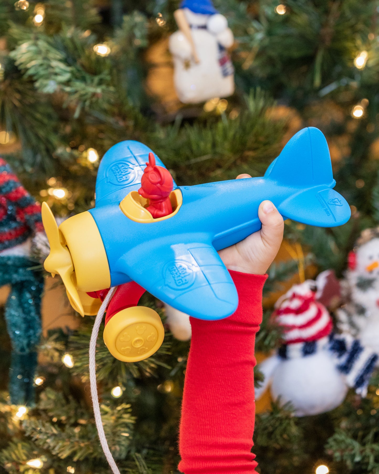 Child's hand holding Mickey Mouse Airplane Pull Toy in front of a Christmas tree