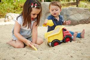 Girl and boy playing in sand with red and yellow Dump Truck